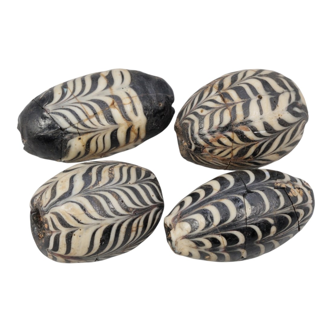 Lot of 4 Antique Islamic Feather-Patterned Glass Beads, Circa 9th-14th Century, 70AD: Comprising four large barrel-shaped beads, ranging from 2.5 cm (1 in.) to 3 cm (1.2 in.), each formed from dark base glass with applied feather-patterned decoration. All beads feature bold black and w