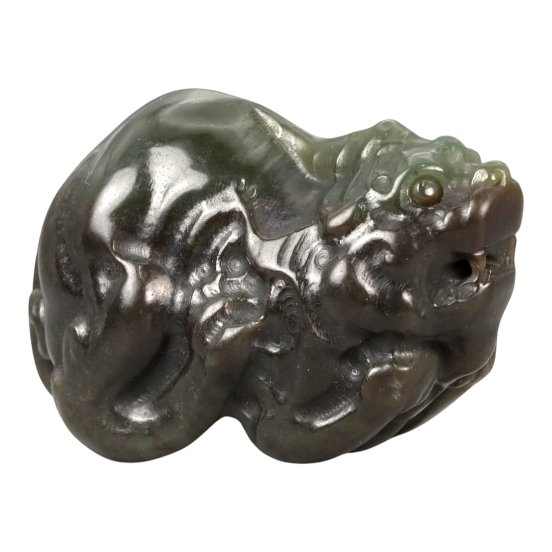 A Chinese Nephrite Jade Pixiu Figure, 20th Century, 87FA: Carved from dark green to olive-toned nephrite jade with areas of translucency and a glossy polish, the figure is modeled as a compact pixiu shown crouching with the body compressed and the head raise