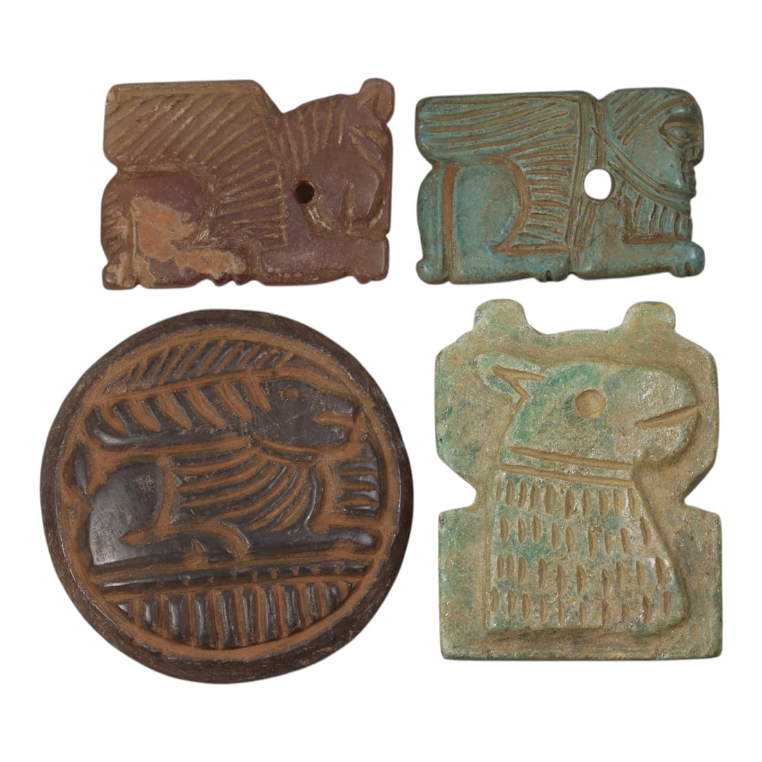 Lot of 4 Ancient Near Eastern Amulets, Circa 1st Millennium BCE, 95AE: Comprising four amulets of varying material and form. One rectangular reddish stone amulet carved with a recumbent feline figure, pierced horizontally for suspension. One rectangular turquoise-glazed 