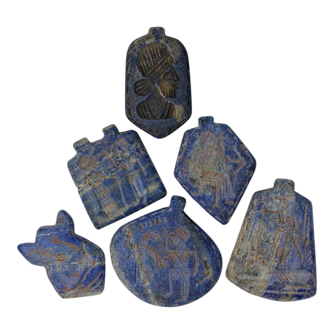 A Lot of 6 Ancient Near Eastern Lapis Lazuli Amulets, 9AC: The group comprises six amulets carved from lapis lazuli, displaying rich blue tones with natural white and grey inclusions, alongside surface patina and wear consistent with antiquity. Each piece fea