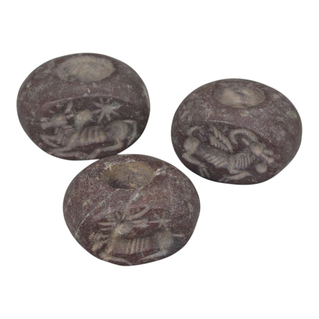 Lot of 3 Sasanian Stone Stamp Seals, Circa 3rd-7th Century CE, 11AG: Comprising three seals carved from dark reddish-brown stone with natural patina and surface wear consistent with age. Each seal is of flattened, disc-shaped form with a central perforation for suspens
