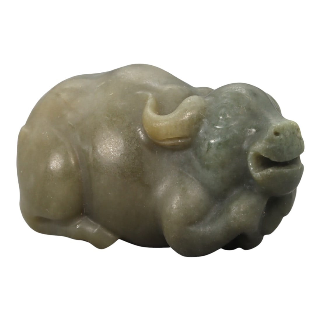 A Chinese Nephrite Jade Buffalo Figure, 20th Century, 97YA: Carved from pale green to buff-toned nephrite jade with areas of soft translucency and natural tonal variation, the figure represents a recumbent buffalo shown in a compact, resting posture. The head 