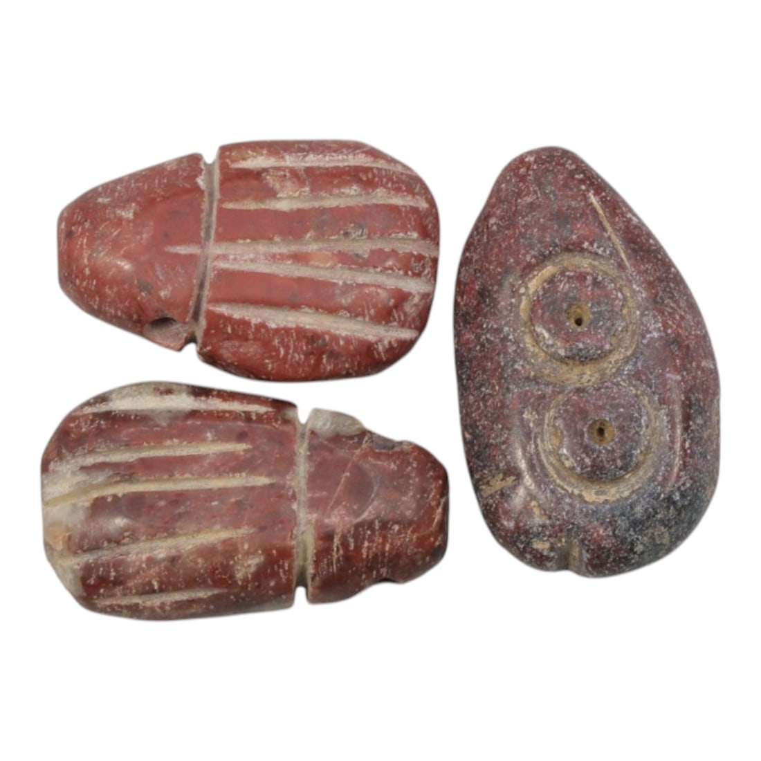 Lot of 3 Ancient Coptic Egyptian Red Stone Amulets, Circa Roman to Coptic Era, 68WL: Carved from variegated red stone, this trio features two stylized scarab amulets with incised elytral detailing and one eye amulet with concentric circle motifs, all exhibiting the simplified craftsma