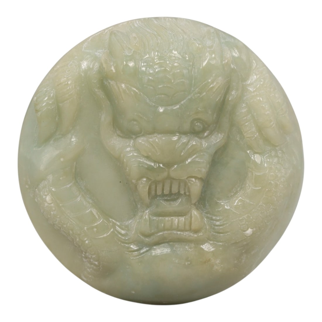 A Chinese Jadeite Jade Dragon Amulet Pendant, 20th Century, 16ZL: Carved from pale green jadeite with subtle tonal variation and a smooth polished surface, the object is formed as a circular disc. The front is decorated in high relief with a dragon head, featuring p