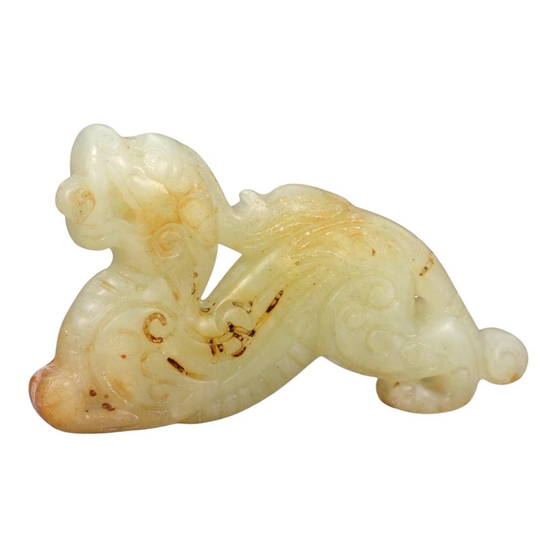 A Chinese Nephrite Jade Chilong Figure, 20th Century, 29FA: Carved from pale celadon nephrite jade with areas of russet skin and natural translucency, the figure is modeled as a recumbent chilong shown in a sinuous, arched posture. The head is raised with a st