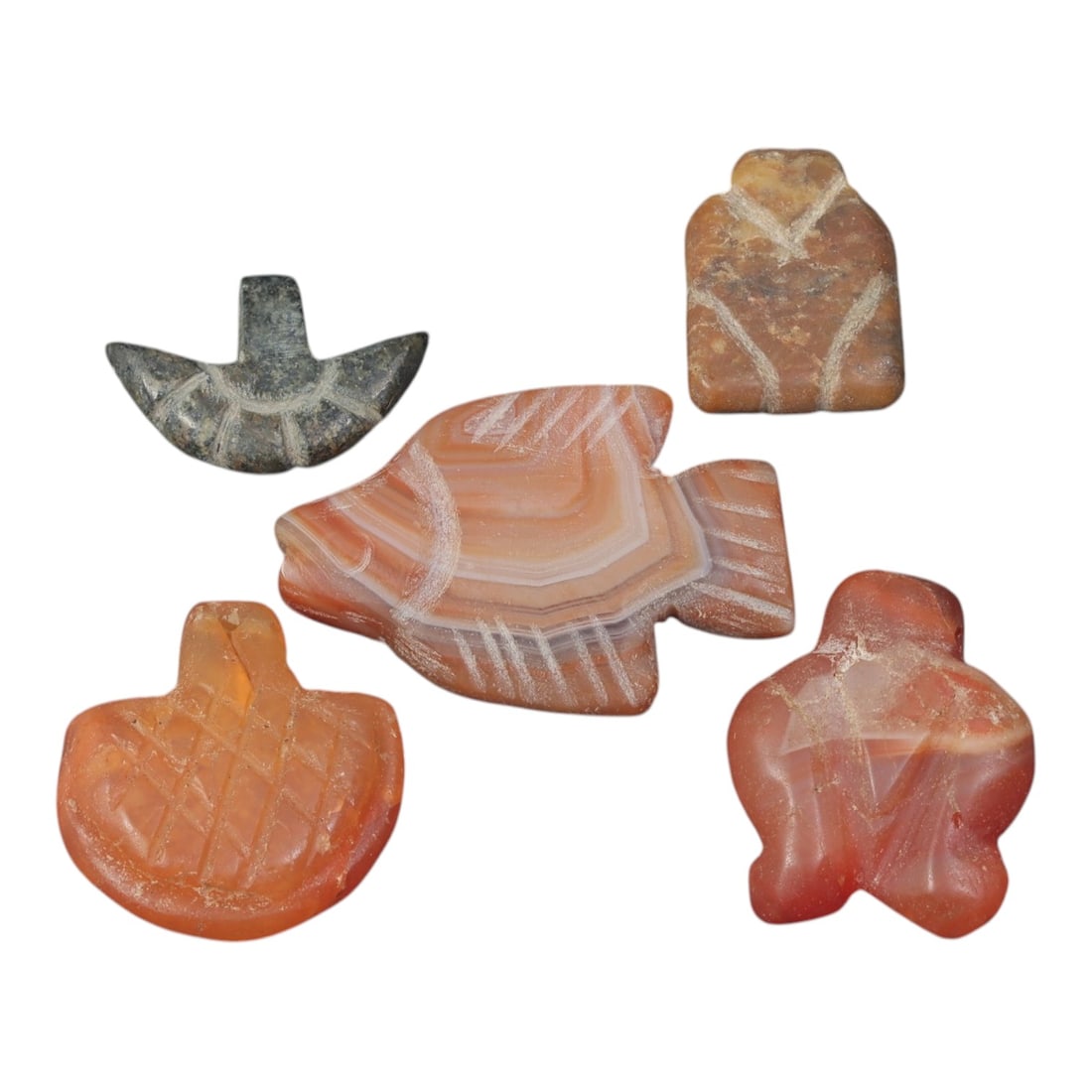 Lot of 5 Ancient Coptic Egyptian Carnelian and Stone Amulets, Circa Roman Period to Coptic Era, 84AD: Comprising five varied amulets ranging from 1.5 cm to 2.5 cm, this collection features pieces carved primarily from carnelian, with one example in dark stone. The designs include stylized fish, bird-l