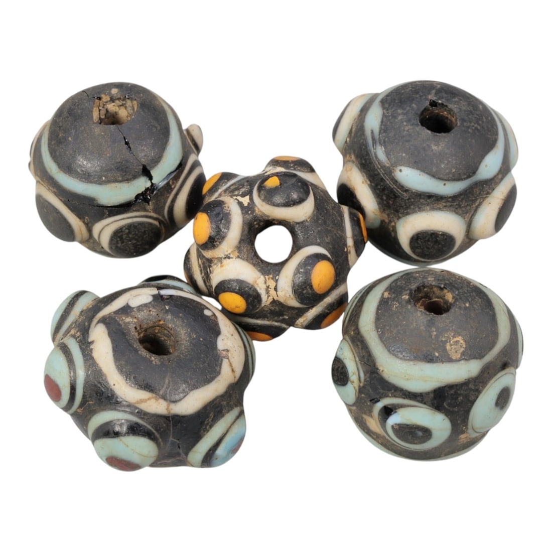 Lot of 5 Antique Islamic Eye-Patterned Glass Beads, Circa 9th-14th Century, 74AD: Comprising five beads of approximately 2 cm (3/4 in.), each formed from dark base glass with raised, applied eye motifs, a common apotropaic design in Islamic glasswork. The beads feature varied color