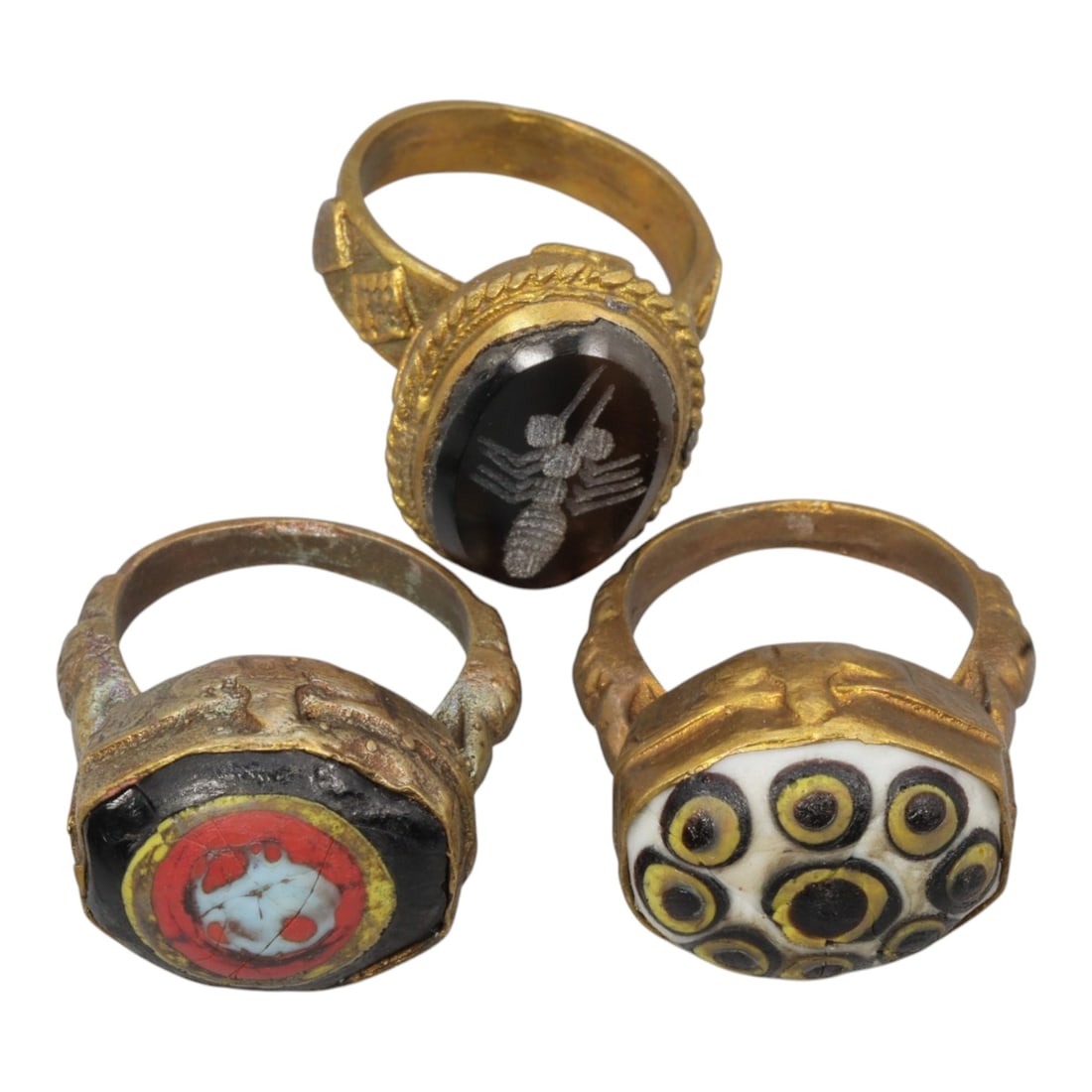 Lot of 3 Antique Qajar Period Gilt Rings, 10AD: This collection features three gilt-metal rings from the Qajar period (19th century), showcasing both intaglio and "evil eye" folk jewelry traditions. One ring has a dark stone engraved with a detaile