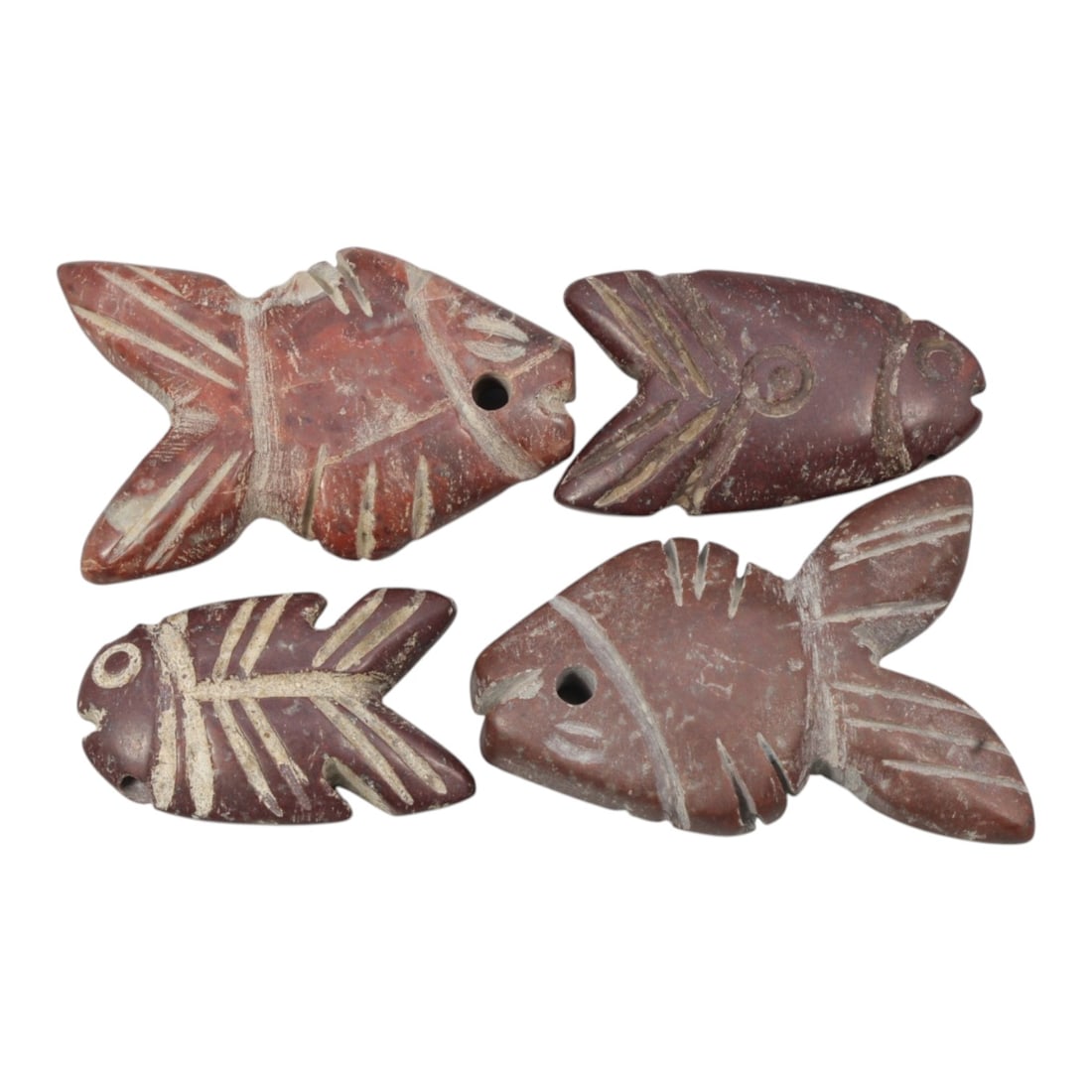 Lot of 4 Ancient Coptic Egyptian Red Stone Fish Amulets, Circa Roman to Coptic Era, 75WL: Carved from rich red stone with contrasting light incised detailing, this set of four fish-shaped amulets features varied stylized fins, tails, and eyes, each with a drilled suspension hole confirming