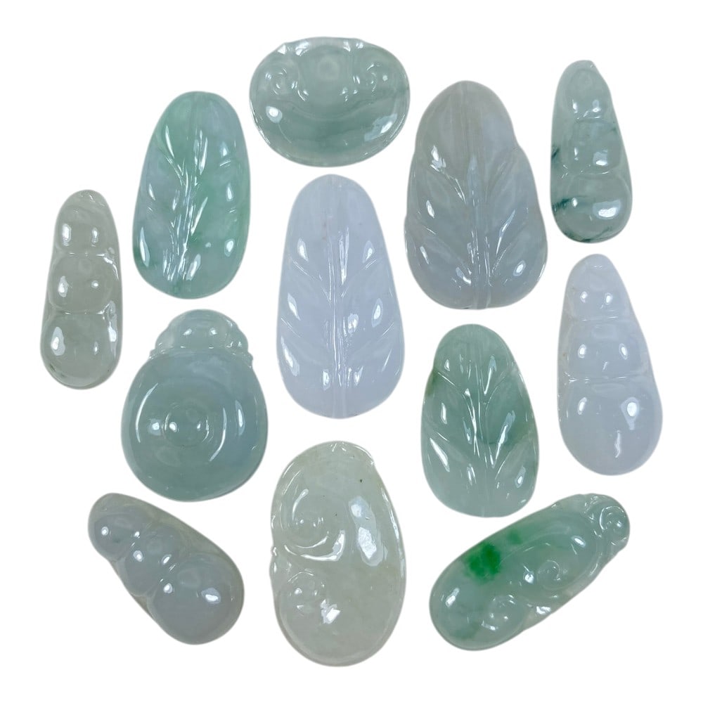 A Lot of 12 Natural Jadeite Jade Carved Pendants, 95AA: This collection features 12 finely carved jadeite jade pendants in translucent tones of pale green, icy white, and lavender. The pieces are carved into auspicious motifs: leaf forms (symbolizing "grea