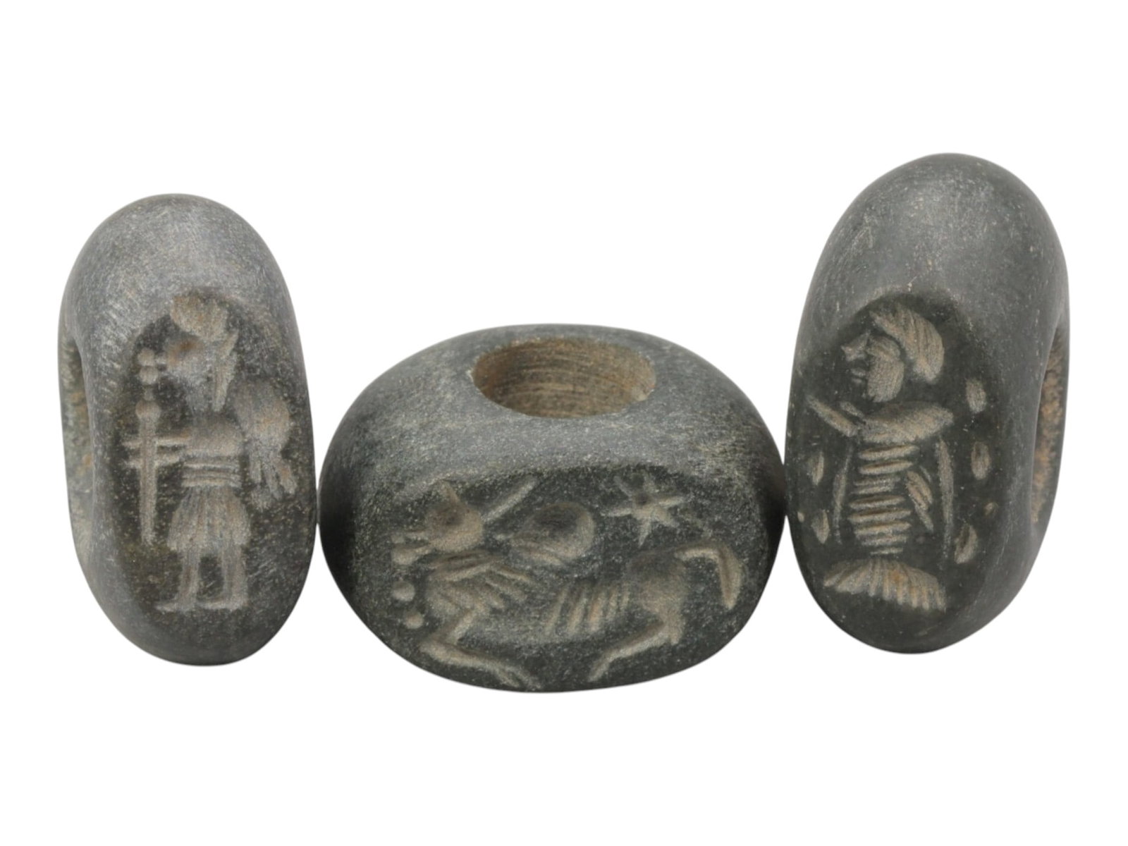 Lot of 3 Sasanian Stone Stamp Seals, Circa 3rd-7th Century CE, 66WM: A group of three Sasanian period stamp seals carved from dark grey stone, each featuring a central perforation for suspension. The seals are incised with distinct motifs typical of Sasanian glyptic ar