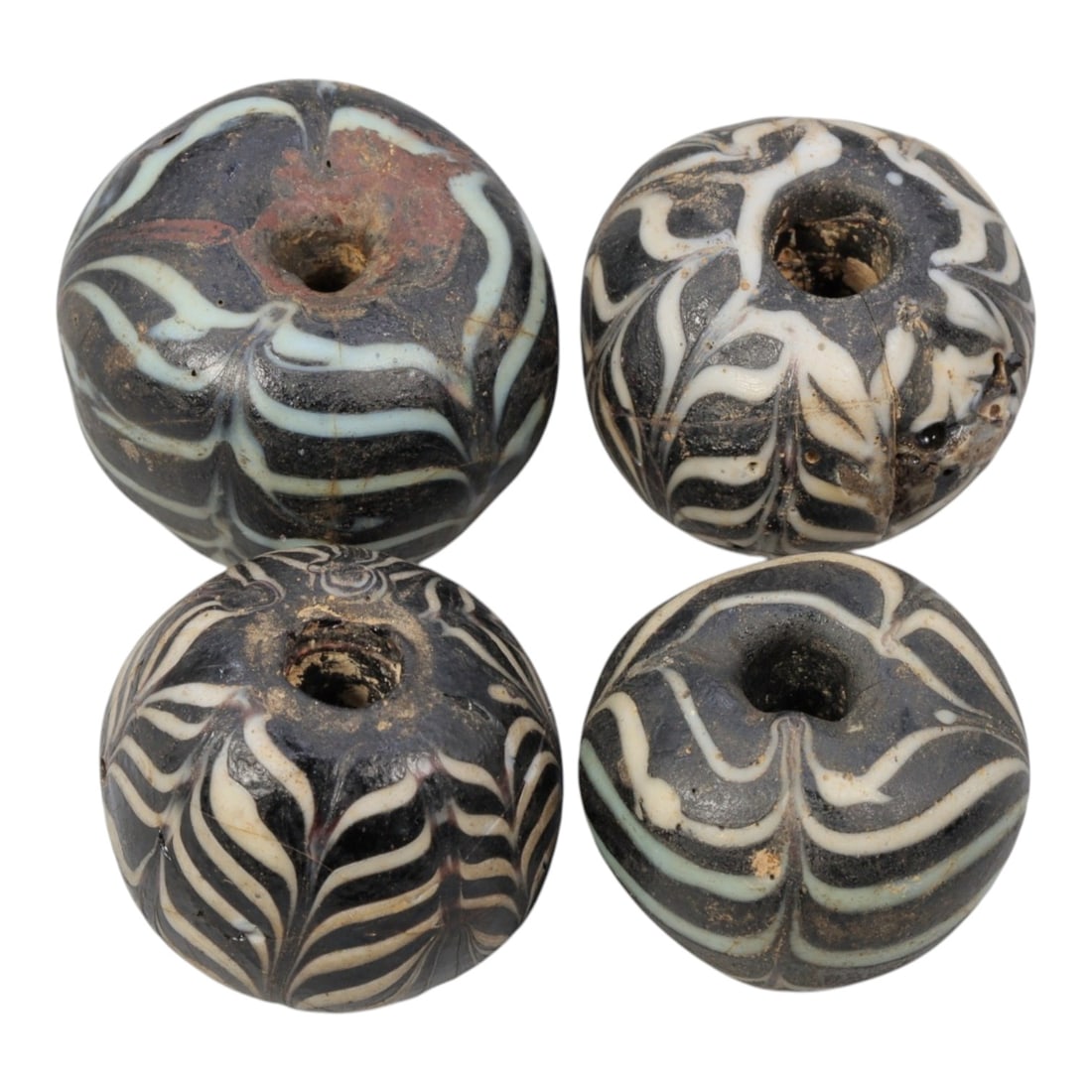 Lot of 4 Antique Islamic Feather-Patterned Glass Beads, Circa 9th-14th Century, 77AD: Comprising four beads ranging from 1.5 cm (5/8 in.) to 2 cm (3/4 in.), each formed from dark base glass with applied feather-patterned decoration. All beads feature black glass cores adorned with whit