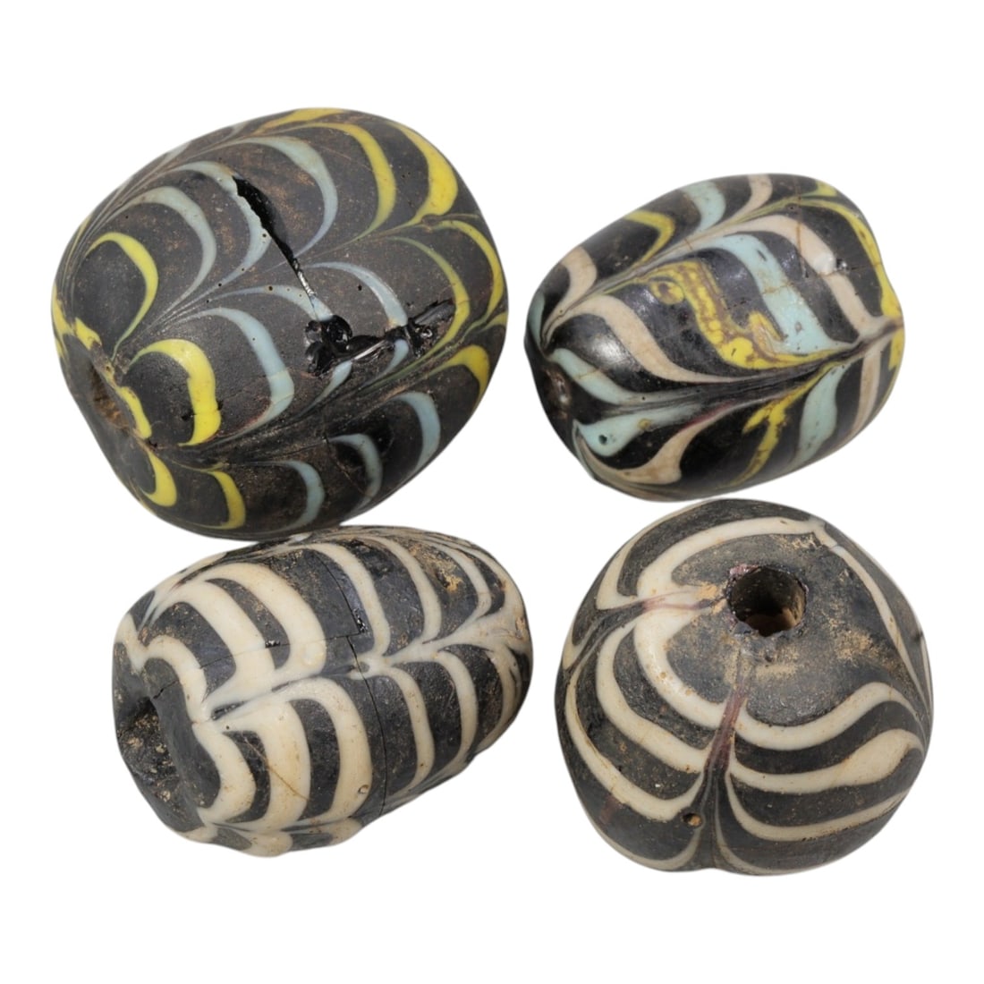 Lot of 4 Antique Islamic Feather-Patterned Glass Beads, Circa 9th-14th Century, 68AD: Comprising four beads of varying sizes, ranging from 2 cm (3/4 in.) to 2.5 cm (1 in.), each formed from dark base glass with applied feather-patterned decoration. Two beads feature black glass with wh