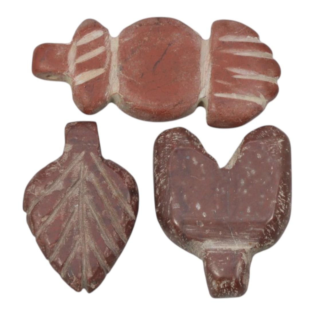 Lot of 3 Ancient Coptic Egyptian Red Stone Amulets, Circa Roman to Coptic Era, 76WL: Carved from rich red stone with contrasting incised detailing, this set includes a composite floral/hand motif pendant, a leaf-shaped amulet with vein incisions, and a stylized bird or heart form, eac