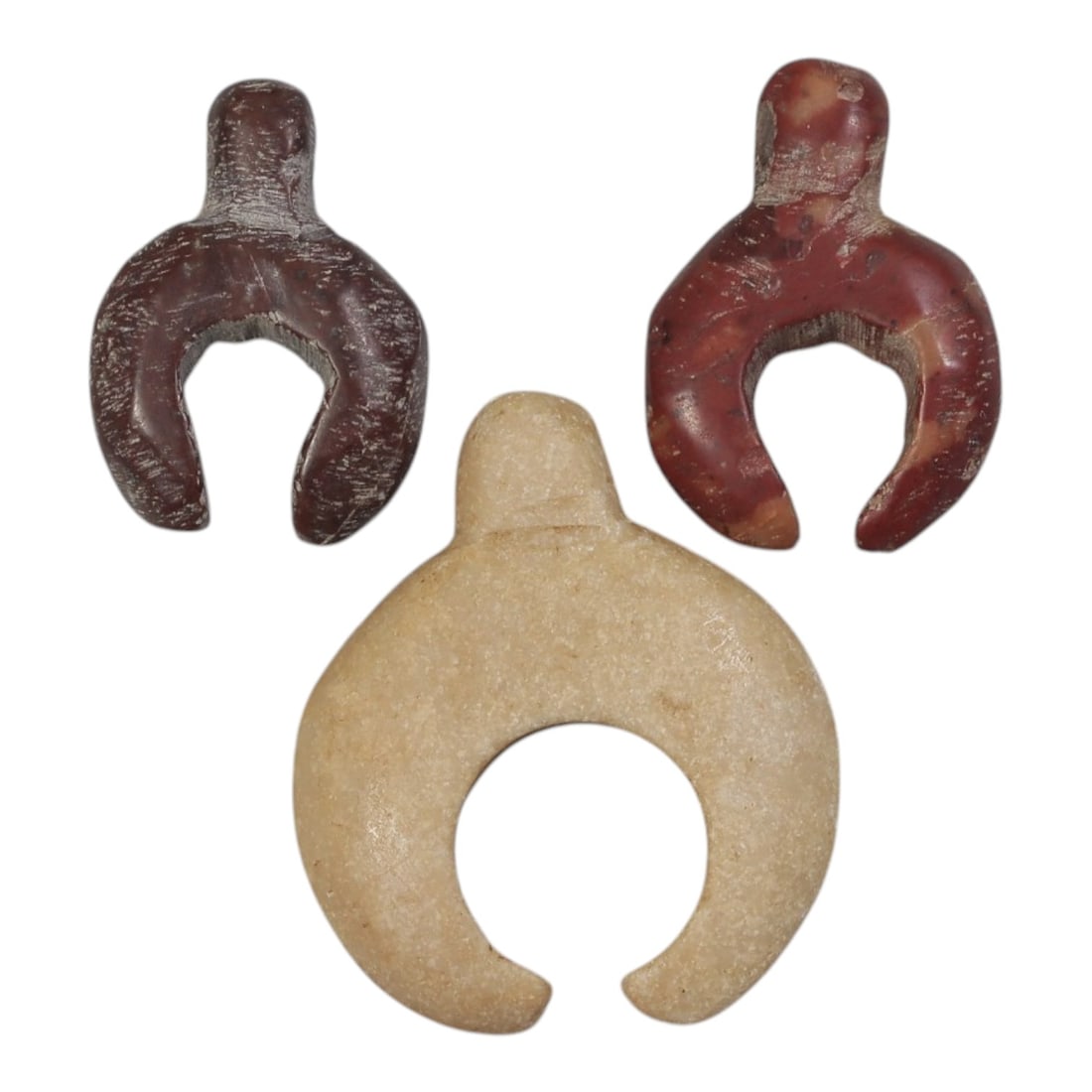 Lot of 3 Ancient Coptic Egyptian Lunar Stone Amulets, Circa Roman to Coptic Era, 73AE: The group comprises three carved stone amulets of lunate form, each with a suspension lug at the top. Two examples are worked from red and reddish-brown stone, while the third is rendered in light bei