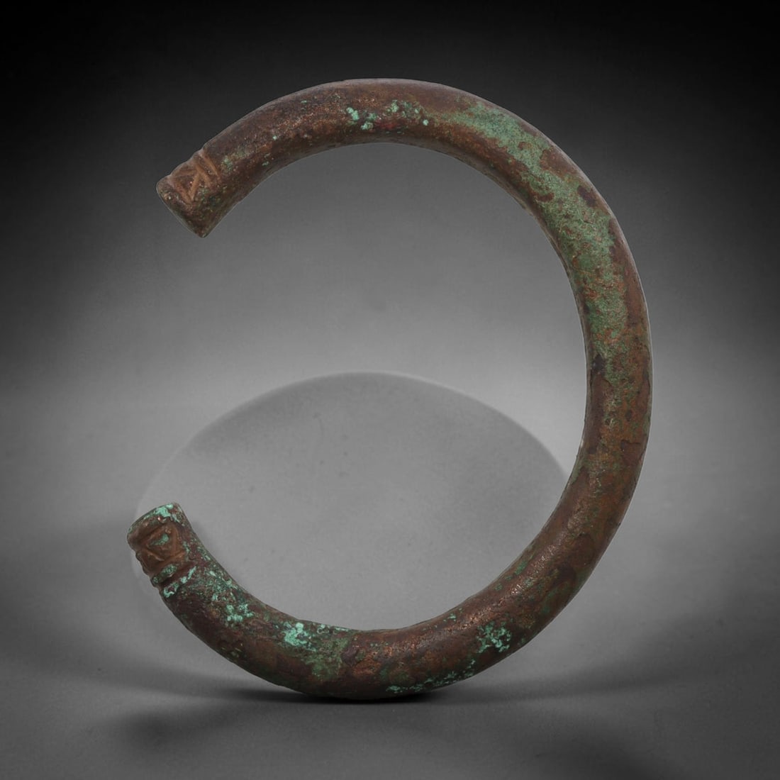 Ancient Bronze Bracelet - Roman Decorated Penannular Bangle, 79BN: A penannular bronze bracelet of ancient Roman origin, formed from a thick, rounded bronze band. The open terminals are decorated with incised geometric motifs, providing subtle detail characteristic o