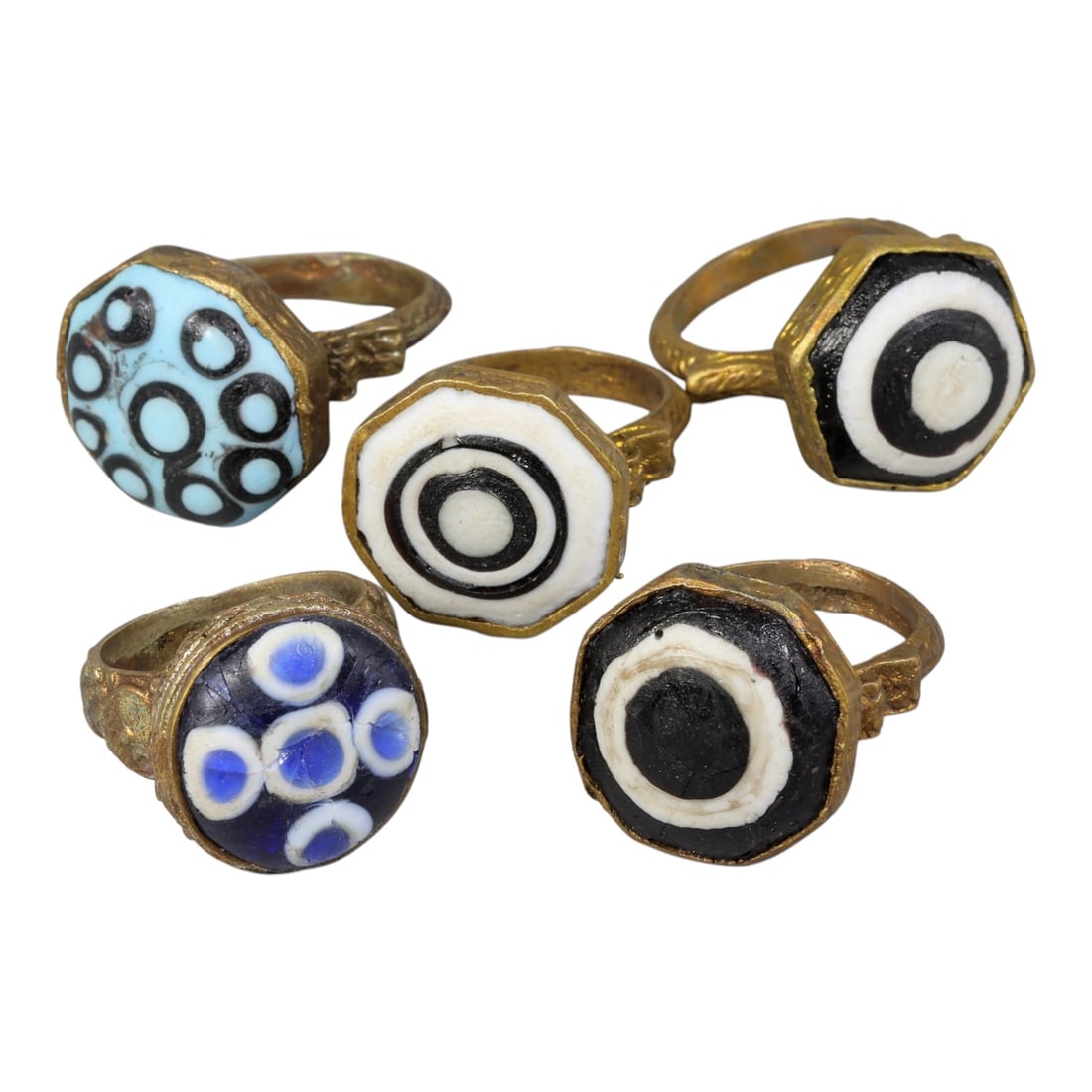 Lot of 5 Antique Qajar Period Gilt Evil Eye Glass Rings, 15AD: A collection of five antique gilt-metal rings from the Qajar period (19th century), each set with a colorful glass "evil eye" cabochon. The glass elements showcase varied patterns and hues, including 