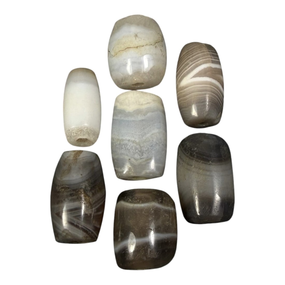 Lot of 7 Himalayan Banded Agate Beads, Ancient to Antique Period, 11AH: A group of seven beads crafted from banded agate, exhibiting natural tonal variations ranging from opaque white and translucent grey to muted brown hues, with characteristic concentric, wavy, and line