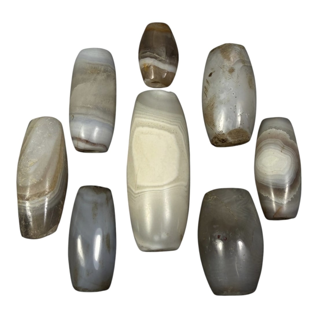 Lot of 8 Himalayan Banded Agate Beads, Ancient to Antique Period, 93AG: A group of eight beads crafted from banded agate, exhibiting natural variations in tone including translucent grey, white, and subtle brownish hues, with characteristic concentric, linear, and wavy ba