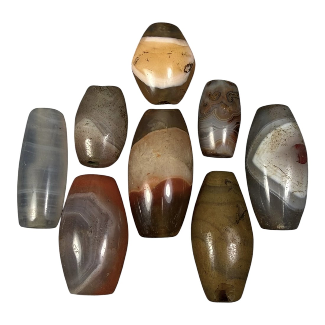 Lot of 8 Himalayan Banded Agate Beads, Ancient to Antique Period, 97AG: A group of eight beads crafted from banded agate, exhibiting natural variations in tone including translucent grey, reddish-brown, yellow, and cream hues, with characteristic concentric, linear, and w