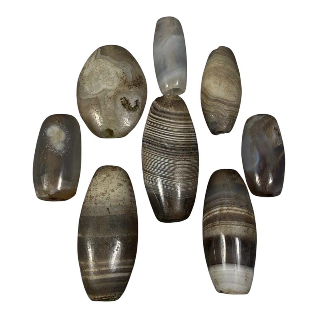 Lot of 8 Himalayan Banded Agate Beads, Ancient to Antique Period, 18AH: A group of eight beads crafted from banded agate, displaying natural variations in tone including translucent grey, brown, and cream hues, with characteristic concentric, linear, and wavy banding patt
