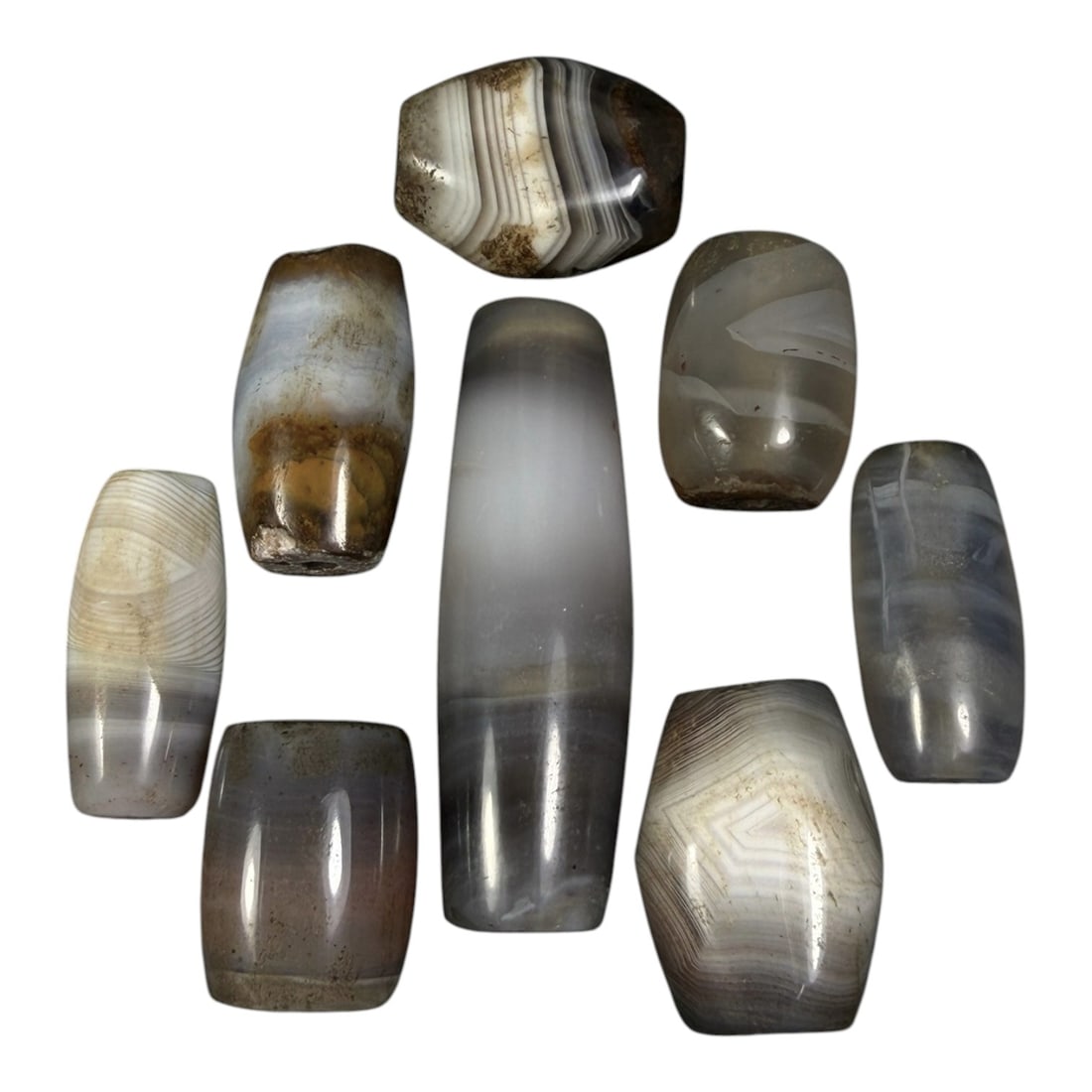 Lot of 8 Himalayan Banded Agate Beads, Ancient to Antique Period, 17AH: A group of eight beads crafted from banded agate, with natural tonal variations ranging from translucent grey and white to muted brown, exhibiting characteristic concentric, wavy, and linear banding p