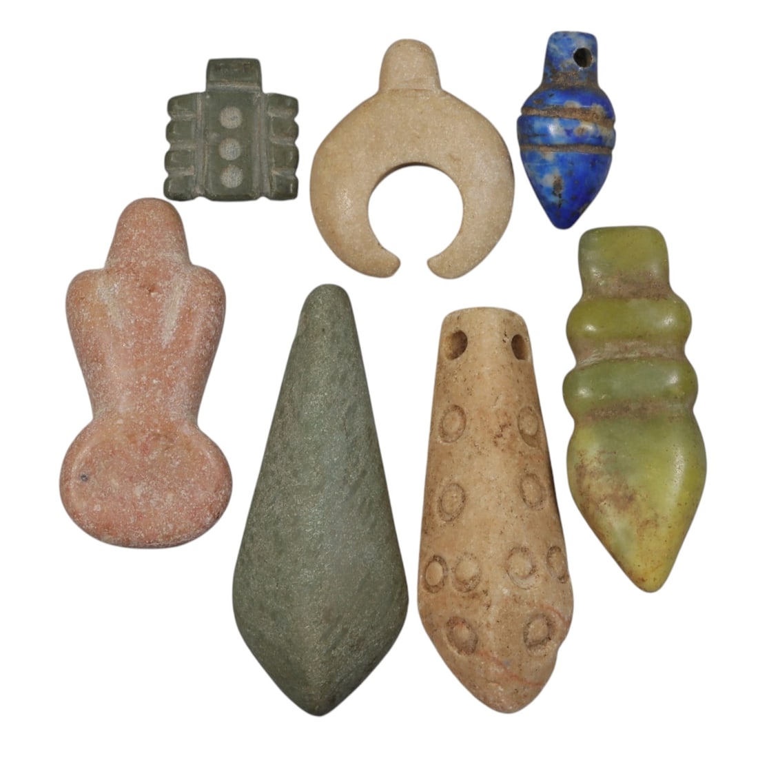 Lot of 7 Ancient Coptic Egyptian Multi-Stone Amulets, Circa Roman to Coptic Era, 99AH: Carved from diverse materials including green serpentine, light beige marble, lapis lazuli, pinkish stone, and yellowish stone, the group consists of seven distinct amulets, ranging in size from 1.5 c