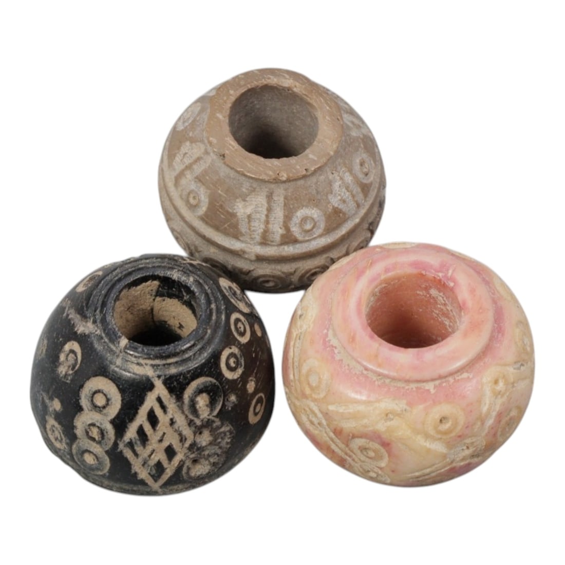 A Lot of 3 Ancient Silk Road Spindle Whorls, 99WK: Three spherical spindle whorls, each carved from different materials and featuring a central perforation for spindle mounting. The examples include a dark stone or bone example with incised geometric 
