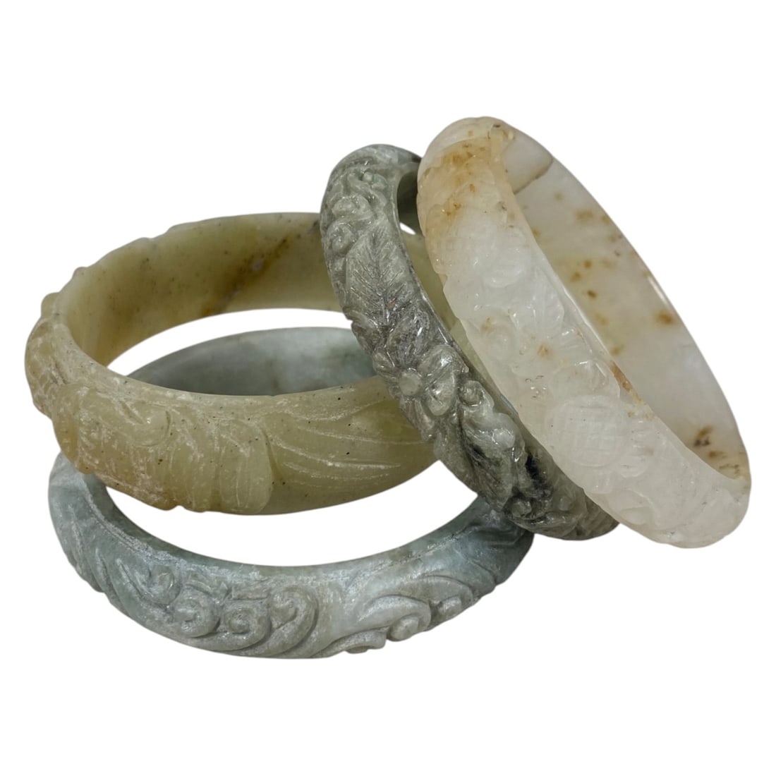 Lot of 4 Chinese Carved Jadeite Jade Bracelets (Bangles), 79AC: Each bracelet is carved from jadeite with varied natural coloration and inclusions, including pale green, grey-green, beige, and off-white with brown mottling. The outer surfaces are decorated with ra