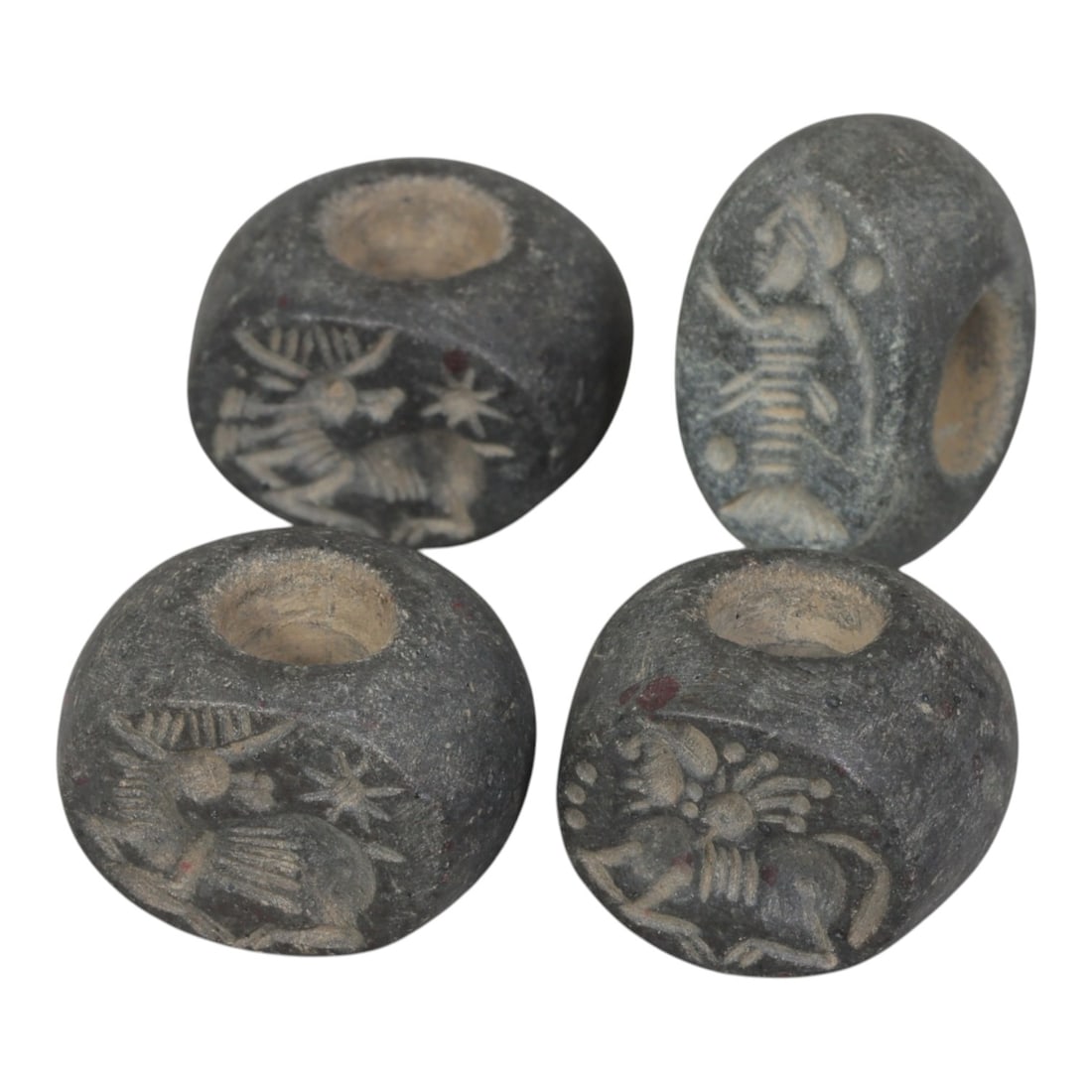 Lot of 4 Ancient Sasanian Stone Stamp Seals, Circa 3rd-7th Century CE, 69WP: A collection of four Sasanian period stamp seals, carved from dark grey stone, each featuring a central drilled hole for suspension. The seals display characteristic Sasanian iconography: including ho