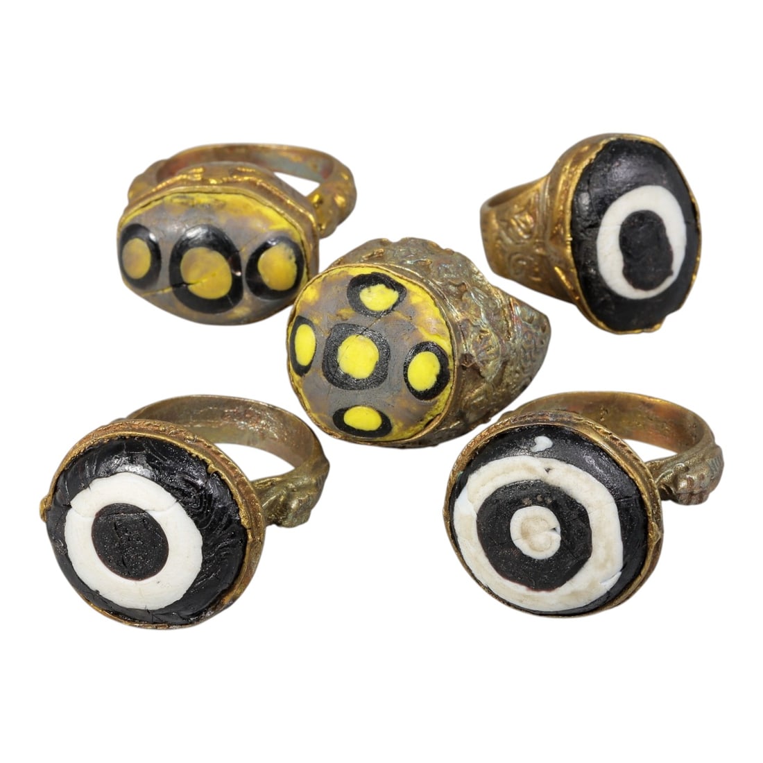 Lot of 5 Antique Qajar Period Gilt Evil Eye Glass Rings, 100AC: A collection of five antique gilt-metal rings from the Qajar period (19th century), each set with a colorful glass "evil eye" cabochon. The set features varied designs: two rings with yellow-and-black