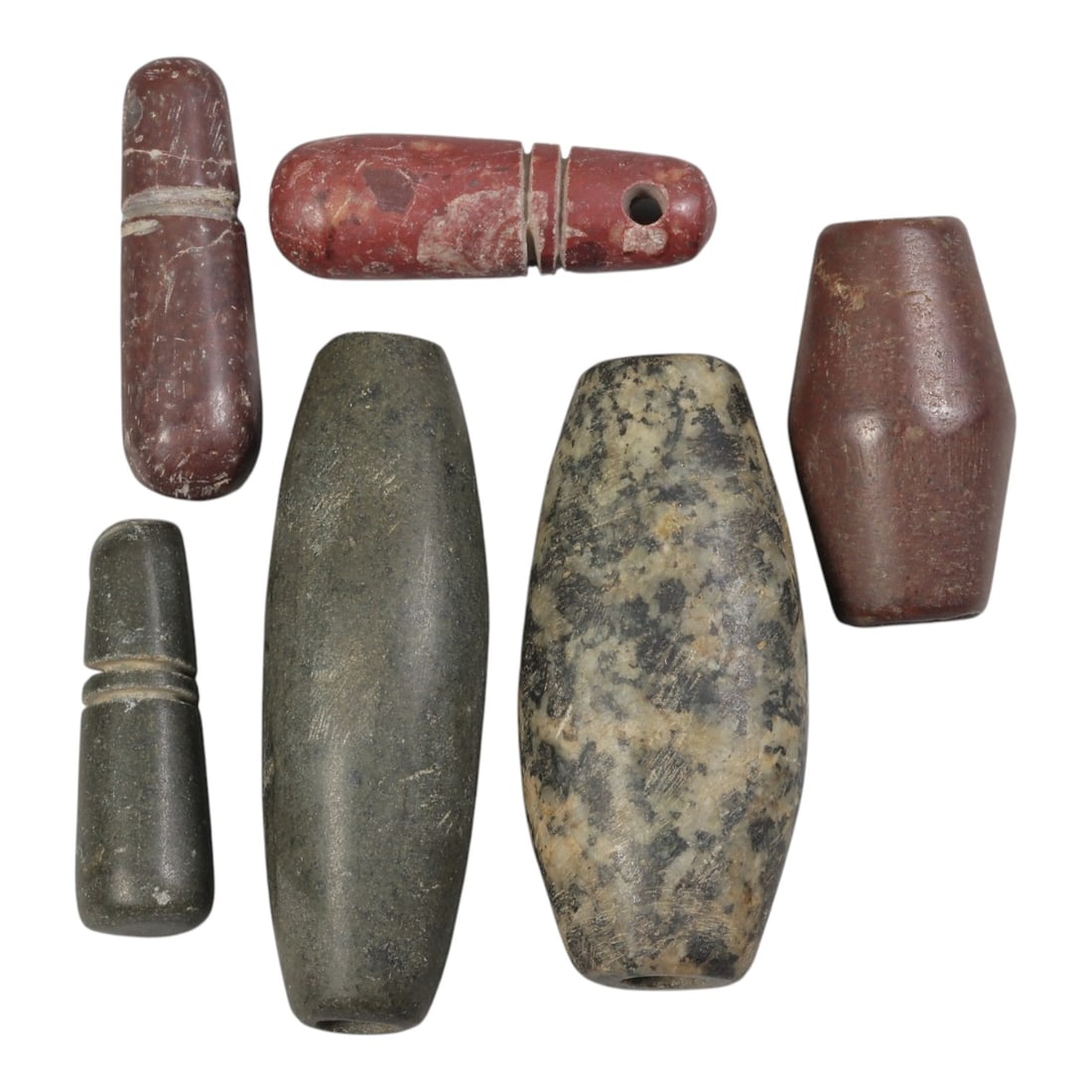 Lot of 6 Ancient Near Eastern Stone Beads, Circa 1st Millennium BCE, 51AE: Comprising six stone beads of varying material, form, and size. The group includes elongated barrel-shaped beads in grey-green, mottled dark and light, and reddish-brown stone. Two reddish examples fe