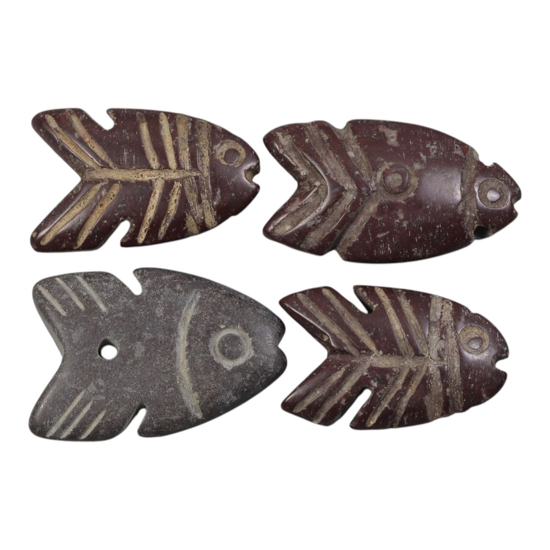 Lot of 4 Ancient Egyptian Stone Fish Amulets, Circa Late Period to Roman Period, 46AE: The group consists of four fish-shaped amulets carved from dark brown and grey stone. Each is rendered in a stylized fish form with incised details representing eyes, scales, and fins. Three examples 