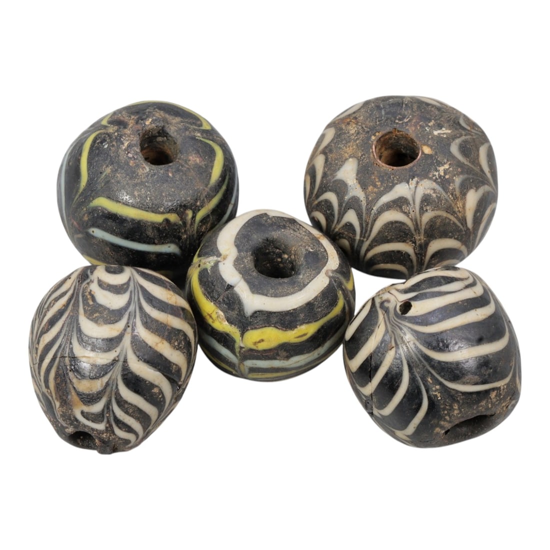 Lot of 5 Antique Islamic Feather-Patterned Glass Beads, Circa 9th-14th Century, 75AD: Comprising five beads of varying sizes, ranging from 1.5 cm (5/8 in.) to 2 cm (3/4 in.), each formed from dark base glass with applied feather-patterned decoration. Three beads feature black glass wit
