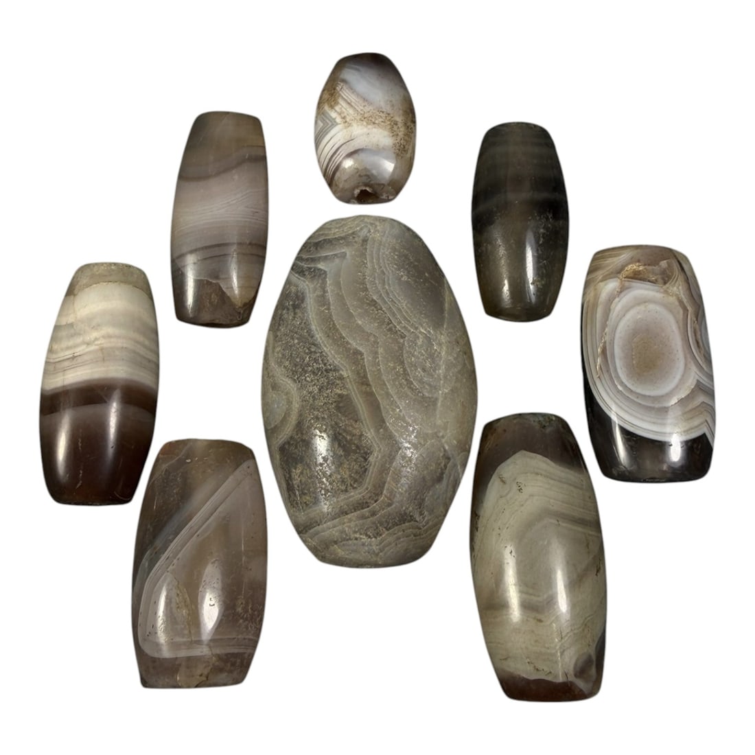 Lot of 8 Himalayan Banded Agate Beads, Ancient to Antique Period, 16AH: A group of eight beads crafted from banded agate, exhibiting natural variations in tone from translucent grey to deep brown, with characteristic concentric and wavy banding patterns. The beads are pri