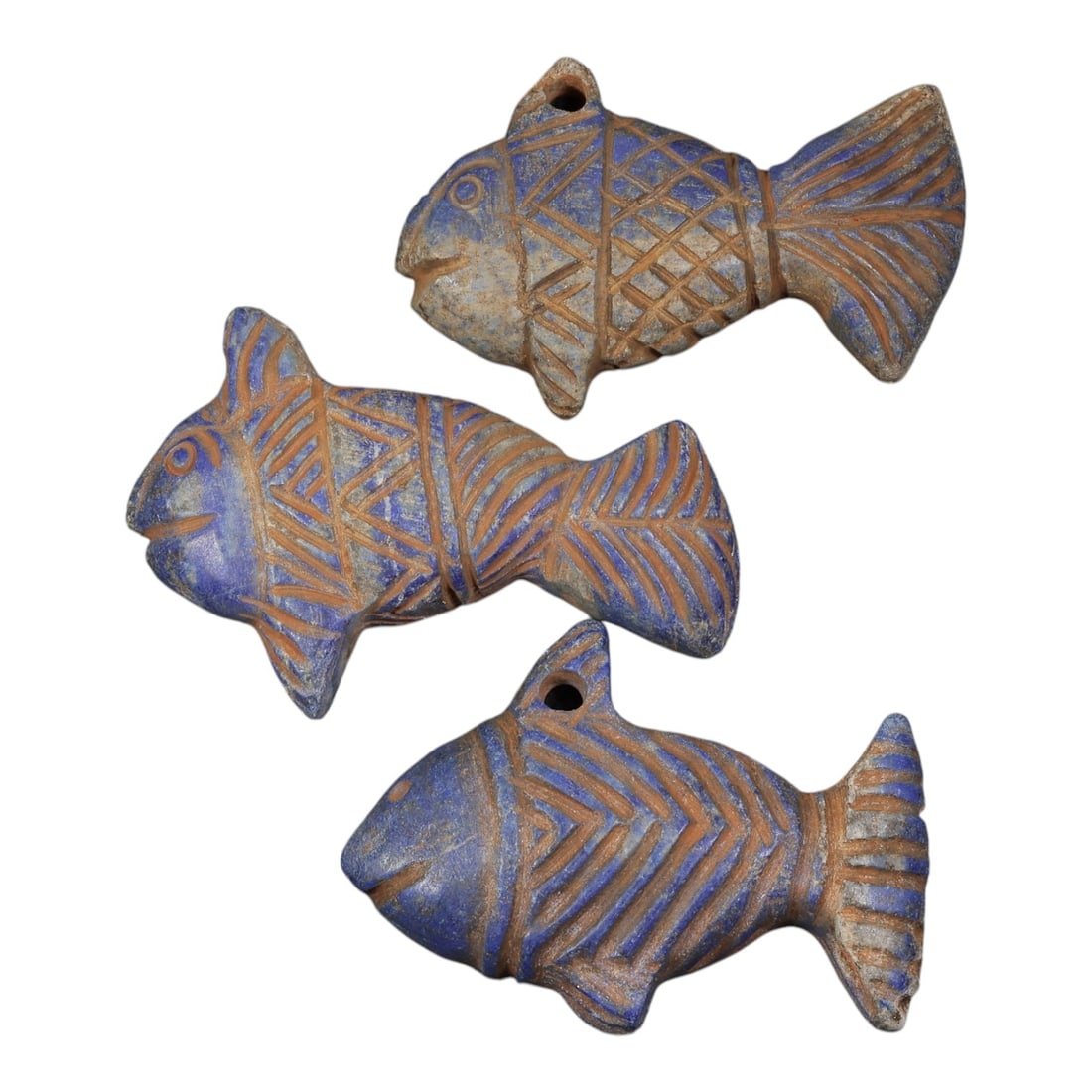 Lot of 3 Ancient Near Eastern Lapis Lazuli Fish Amulets, Circa 1st Millennium BCE, 95AD: Comprising three fish-shaped amulets carved from lapis lazuli, each with stylized incised decoration. The bodies are adorned with geometric patterns including crosshatching, chevrons, and linear stria