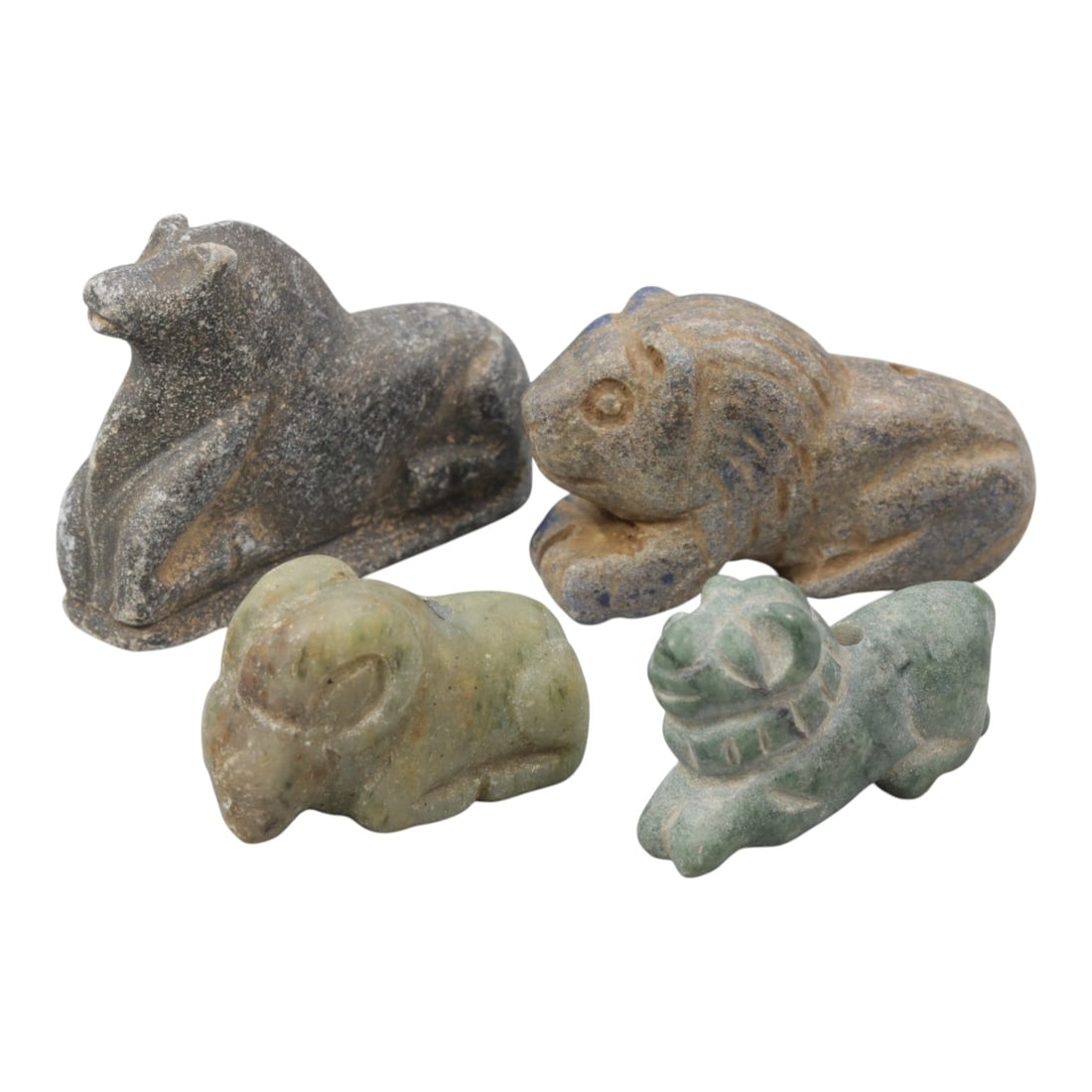 Lot of 4 Ancient Near Eastern Zoomorphic Stone Effigies, Circa Iron Age, 2AE: The group comprises four zoomorphic effigy amulets carved from various stones, including grey schist, lapis lazuli, and greenish stone. The figures depict recumbent animals: a bovine, a lion, a ram, a