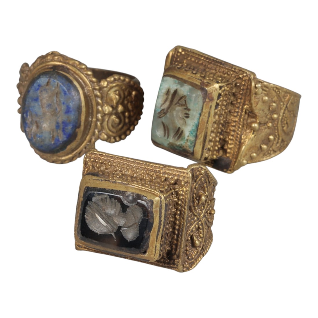 Lot of 3 Antique Qajar Period Gilt Intaglio Signet Rings, 62WP: A collection of three antique signet rings from the Qajar period, each featuring an ornate gilt metal setting with intricate granulation and filigree detailing. The rings are set with different intagl