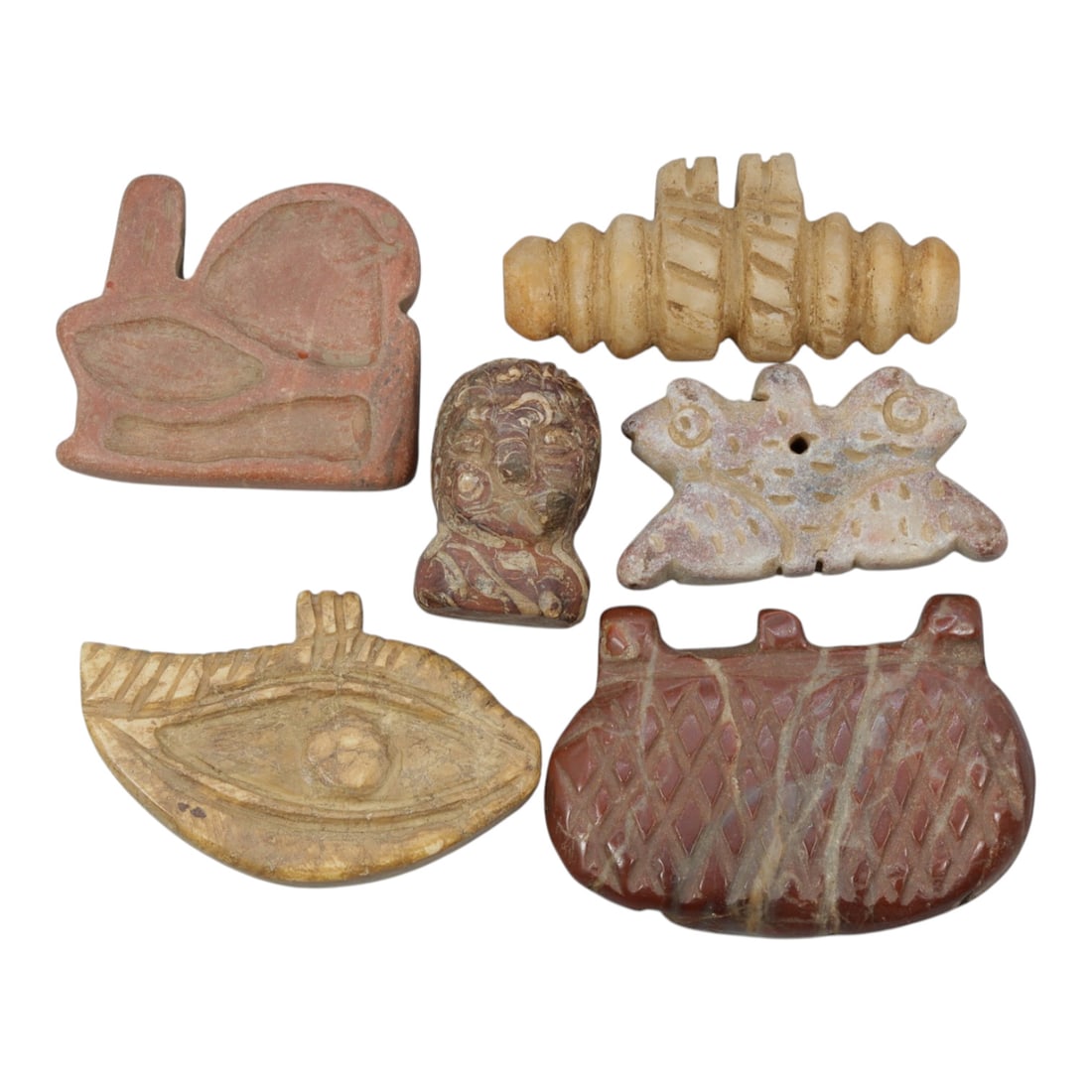 Lot of 6 Ancient Near Eastern Stone Amulets, 80WP: A collection of six ancient stone amulets, carved from varied materials including red, beige, and light-toned stone. The set includes: a stylized bird pendant, a ribbed cylindrical bead, a small carve