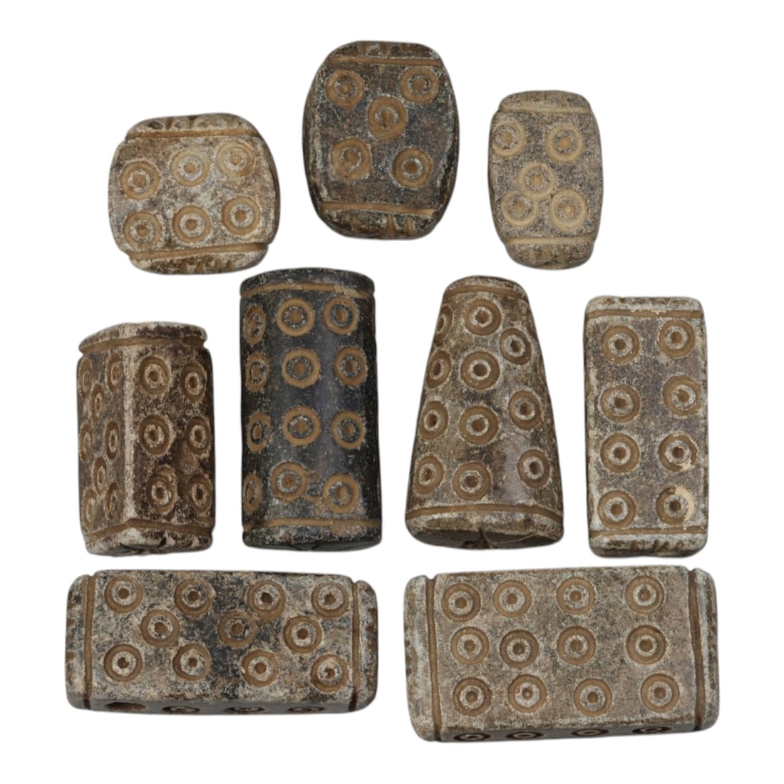 Lot of 9 Ancient Schist Beads with Incised Concentric Circles, Circa Early First Millennium BCE,: Carved from dark grey schist with natural patination, the group consists of nine beads of varying forms, including rectangular, cylindrical, trapezoidal, and oval examples. Each piece is decorated wit