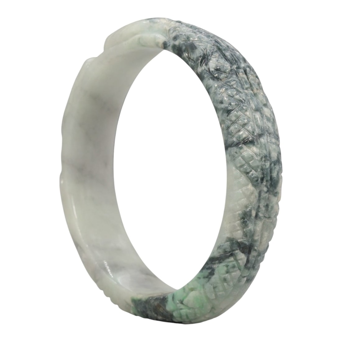 A Chinese Carved Jadeite Jade Bangle Bracelet, 20th Century, 27ZL: A fine jadeite bangle of circular form, masterfully carved in relief with a continuous band of a sinuous dragon coiling around its circumference. The stone exhibits a striking variegated palette, with