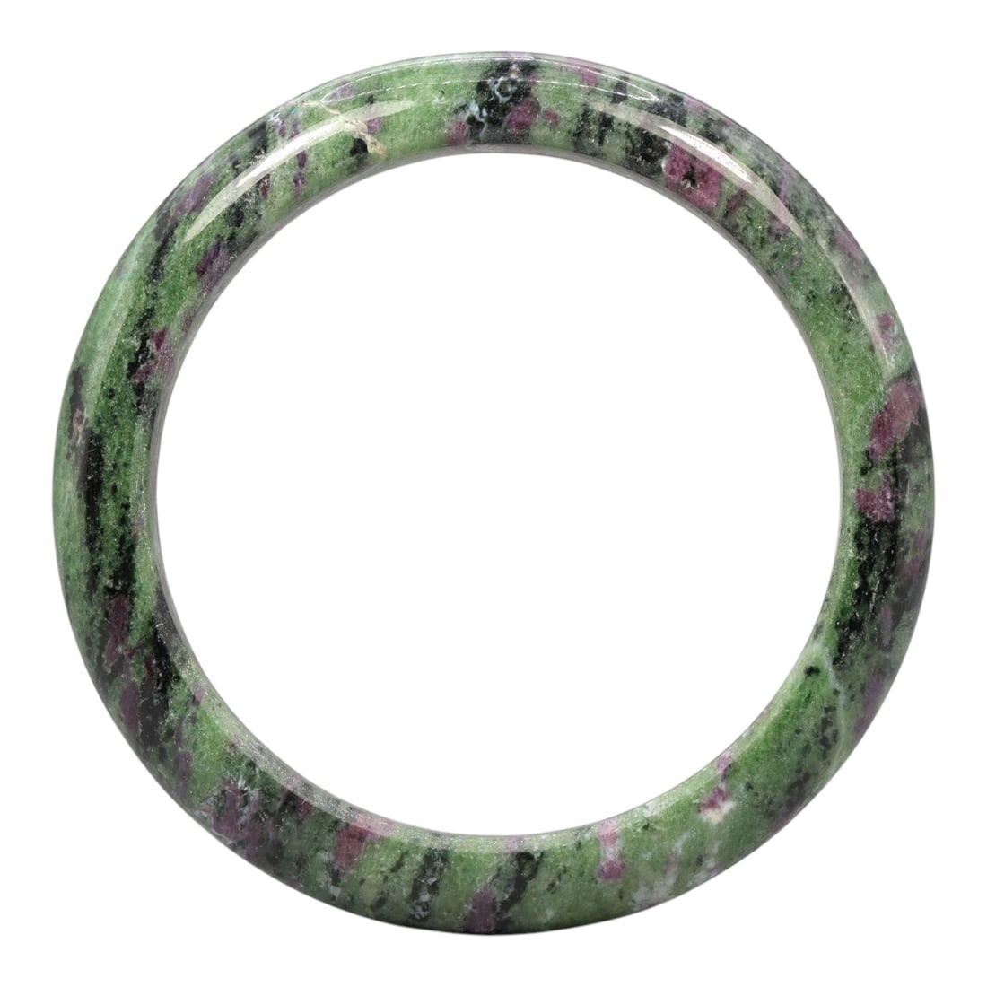 A Ruby Zoisite Bangle, 20th Century, 1ZK: Carved from ruby zoisite, this bangle is formed as a continuous circular band with a rounded, slightly thickened profile. The material exhibits a vibrant green zoisite matrix, with distinct black incl