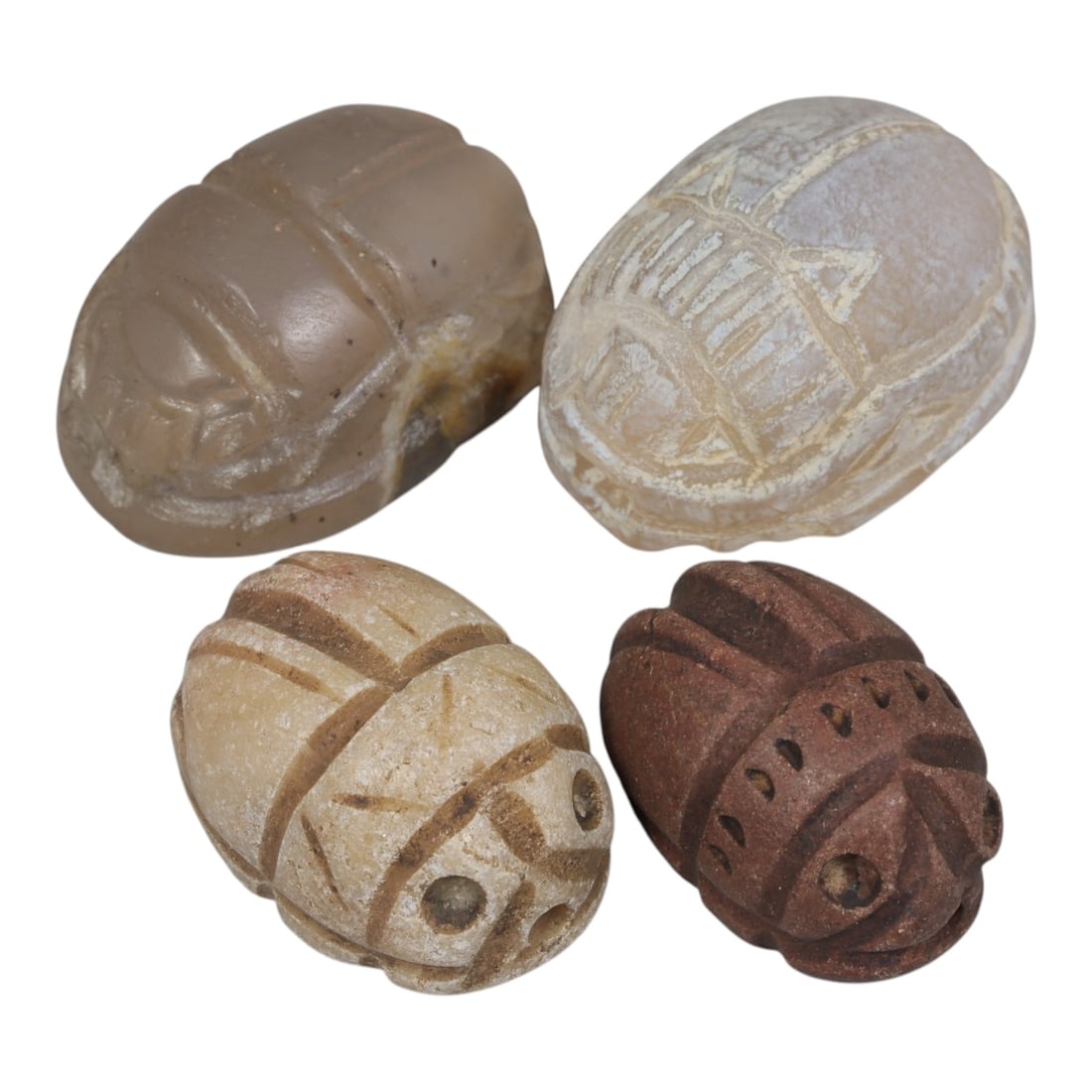 Lot of 4 Ancient Coptic Egyptian Stone Scarabs, Circa Roman to Coptic Era, 66AE: The group comprises four scarab amulets carved from stone in varying tones of light grey, off-white, beige, and reddish-brown. Each is rendered in the traditional scarab form, with incised lines defin