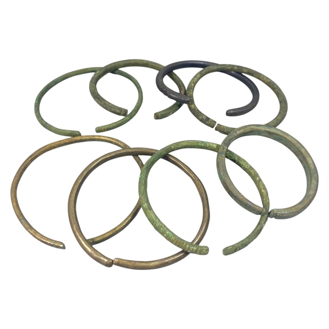 Lot of 8 Roman Bronze Bracelets, Circa 1st-4th Century CE, 94AC: Each bracelet is formed from a single length of bronze, hammered into a circular band with open, overlapping terminals. The metal exhibits varied patination, including green, brown, and dark surfaces,