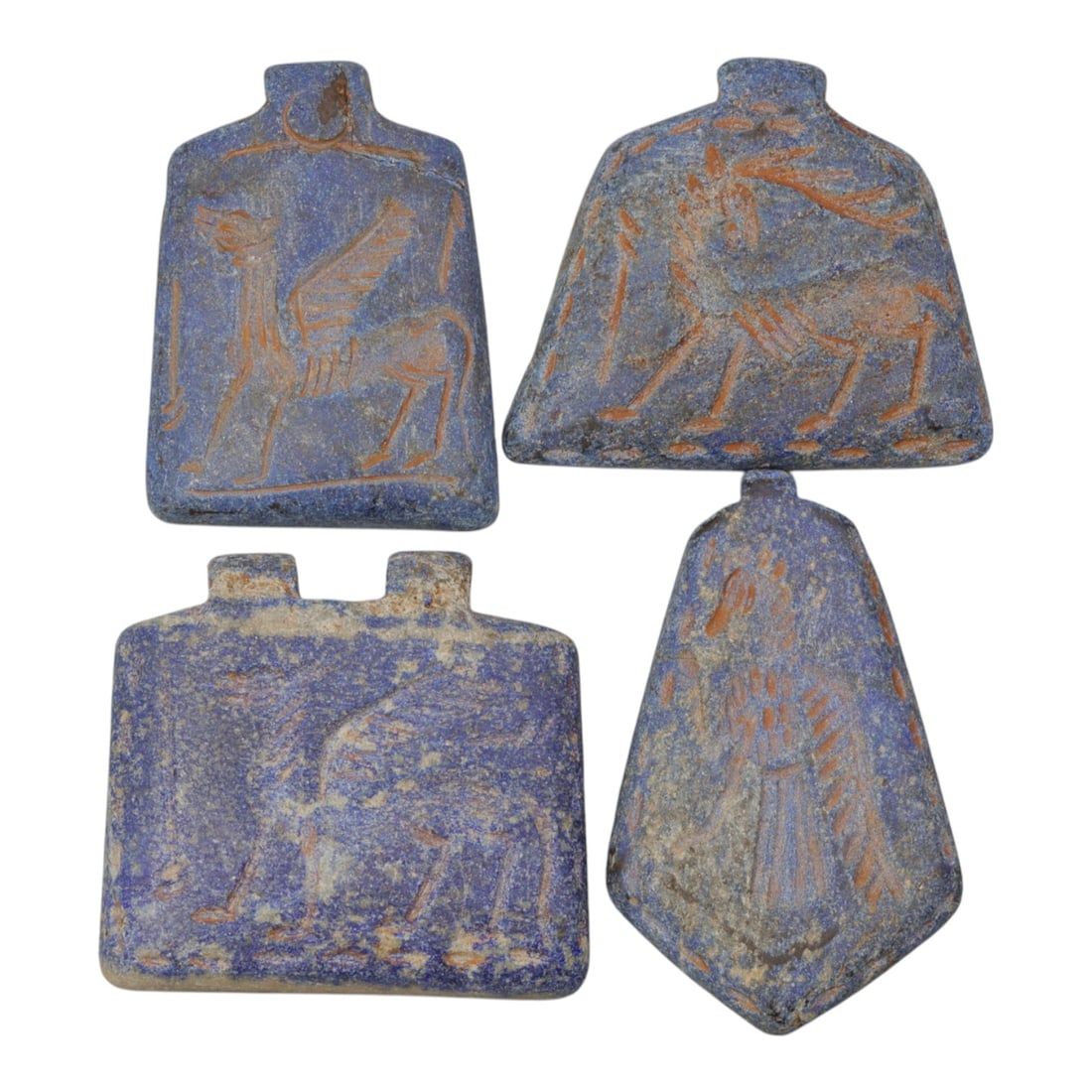 A Lot of 4 Ancient Near Eastern Lapis Lazuli Amulets, 98WM: A curated lot of four ancient Near Eastern-style amulets, carved from lapis lazuli stone. Each piece features incised decoration in reddish pigment, depicting mythical and zoomorphic figures including