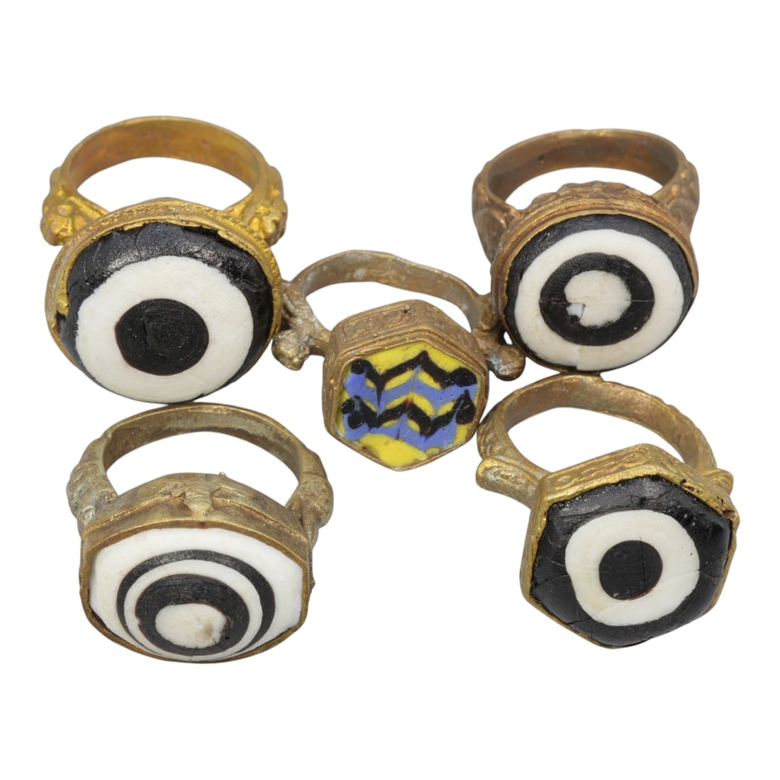 Lot of 5 Antique Qajar Period Gilt Evil Eye & Decorative Glass Rings, 6AD: This collection includes five gilt-metal rings from the Qajar period (19th century), each set with colorful glass cabochons reflecting traditional folk jewelry motifs. Most rings feature classic black