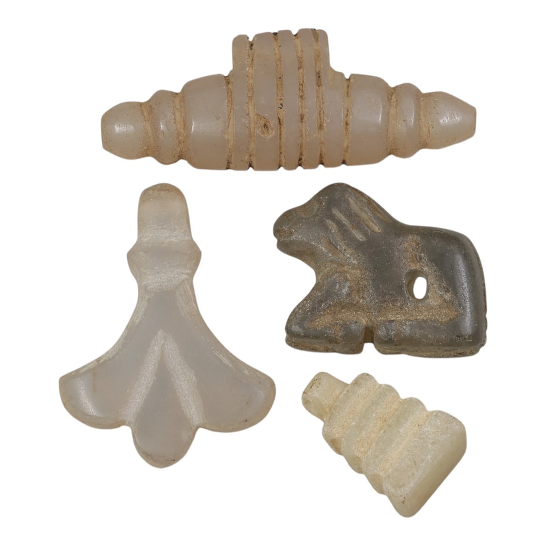 Lot of 4 Ancient Coptic Egyptian Stone Amulets, Circa Roman to Coptic Era, 68AE: The group comprises four carved stone amulets of varied forms, including zoomorphic, geometric, and stylized botanical types. The pieces are worked in translucent white, light grey, and pale stone, wi
