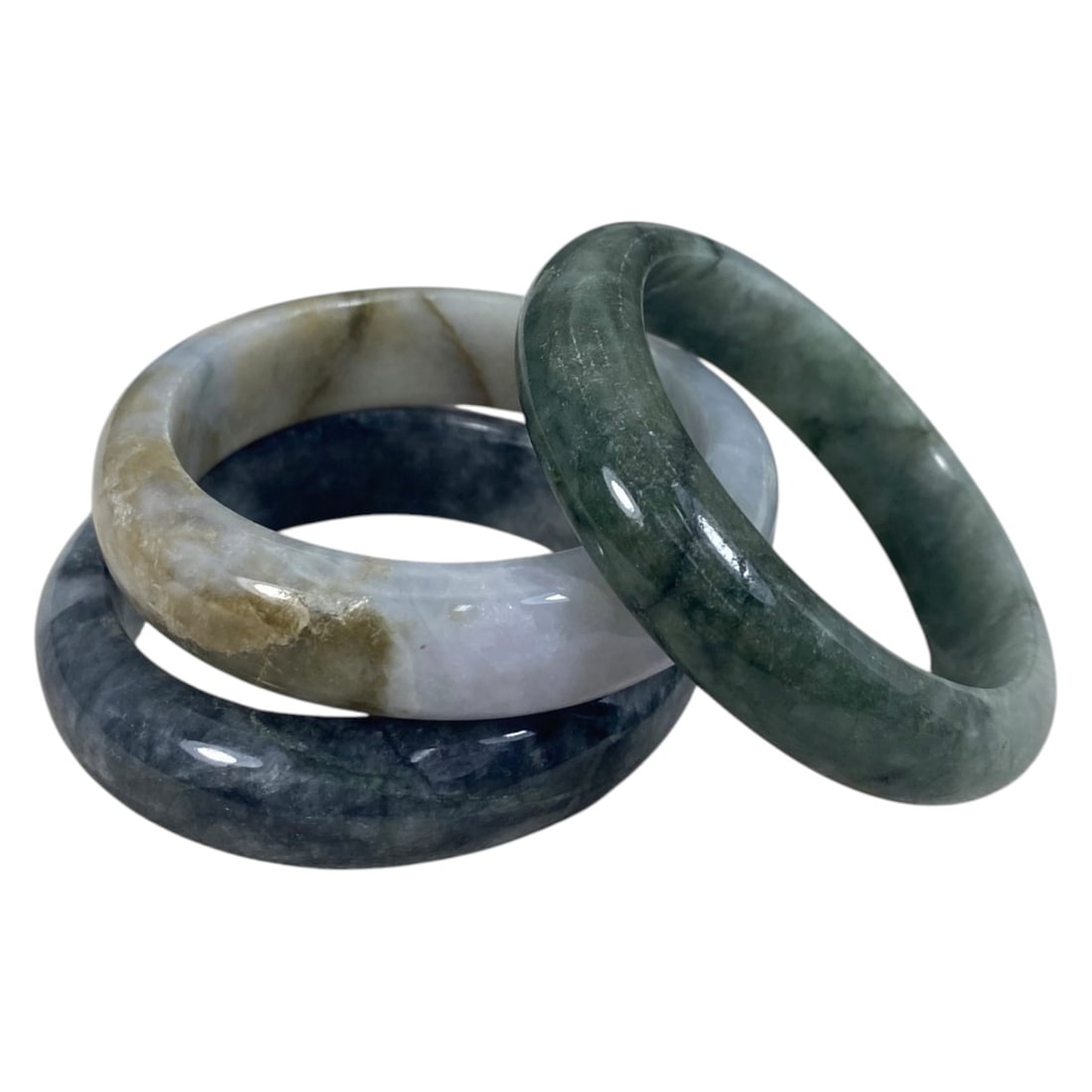 Lot of 3 Chinese Polished Jadeite Jade Bracelets (Bangles), 82AC: Each bracelet is a smooth, uncarved circular bangle crafted from jadeite. The pieces exhibit varied natural coloration and inclusions, including deep grey-blue with clouded patterning, light lavender-