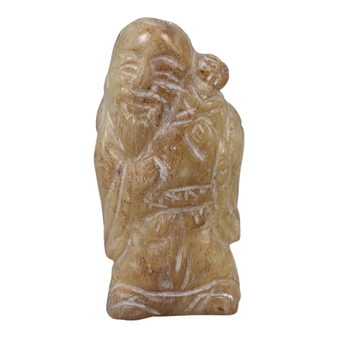 A Chinese Hetian Jade Figure, 20th Century, 84FH: Carved from warm brown-toned Hetian nephrite jade with lighter striations and natural inclusions, the small figure is rendered standing and carved in the round. The subject is depicted as a bearded ma