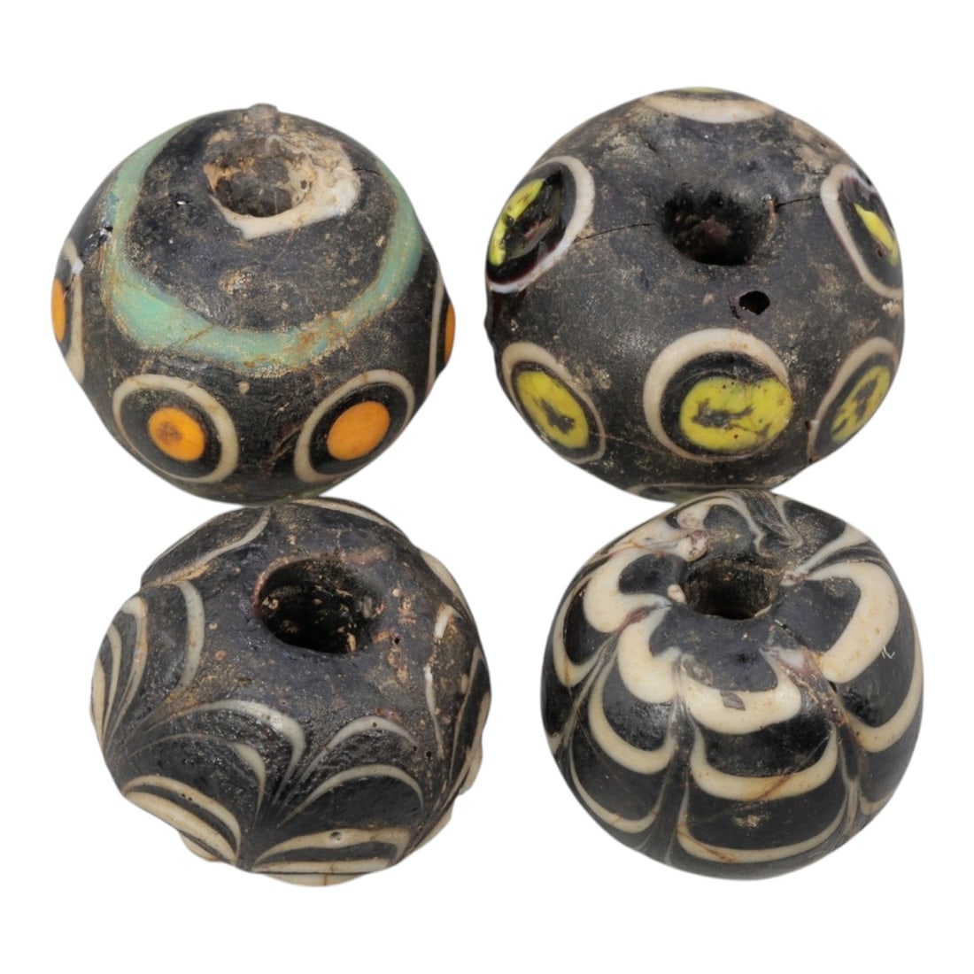 Lot of 4 Antique Islamic Glass Beads, Circa 9th-14th Century, 76AD: Comprising four beads ranging from 1.5 cm (5/8 in.) to 2 cm (3/4 in.), each formed from dark base glass with varied decorative motifs. Two beads feature eye-like concentric circle designs, a common ap